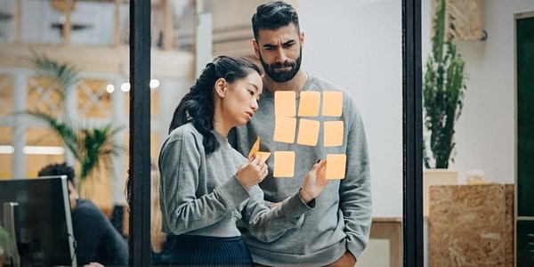 Two professionals going over sticky notes on a glass meeting board
