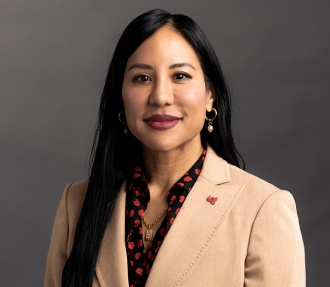 Dr. Raelene Brooks wearing a camel-colored blazer, a black and red shirt and a red phoenix pin on her jacket lapel.