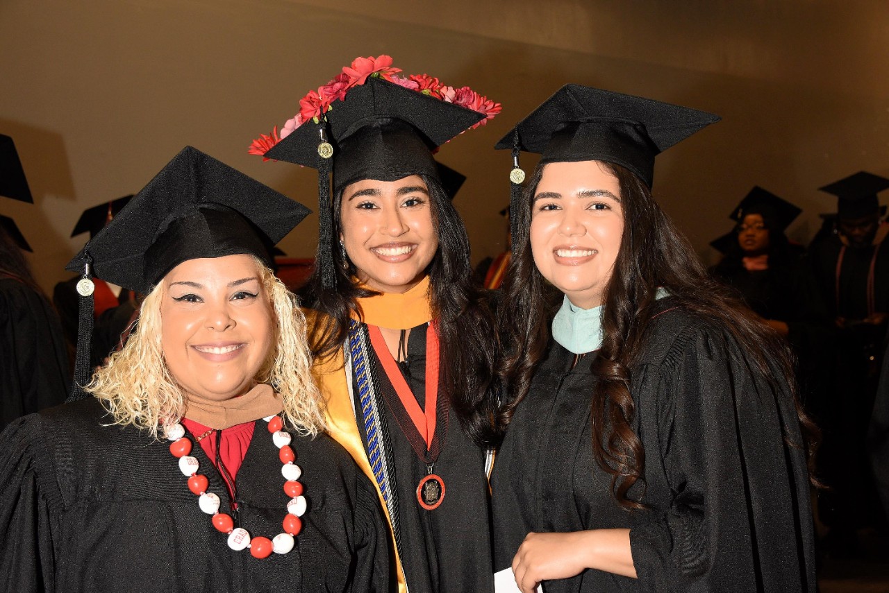 Three graduates stand together wearing caps and gowns for the 2025 University of Phoenix Las Vegas commencement ceremony.