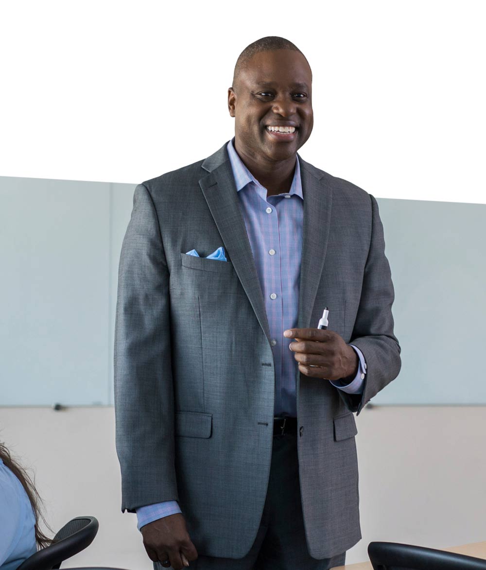 Faculty member in formal attire addressing an audience during a meeting.