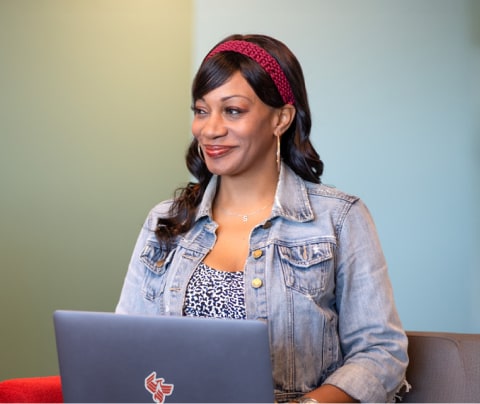 A student smiling and staring out of a window with a laptop in their lap