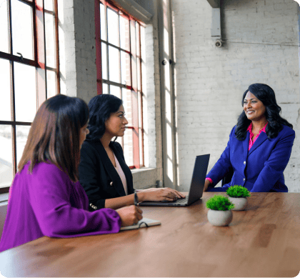 Person in a blue blazer discusses their dissertation with two committee members at a conference table for an online DBA defense.