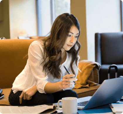 A student works on a laptop in a comfortable study space while refining their online DBA research problem. 