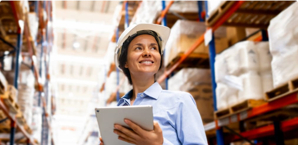 A confident woman in a hardhat in a warehouse setting, symbolizing skill development and career growth in a professional setting.