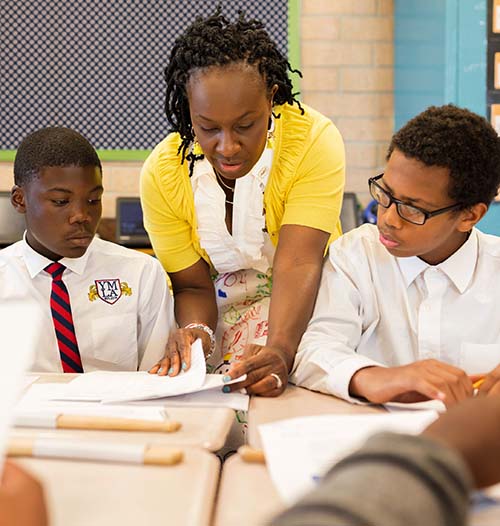 Teacher teaching two students at their desk