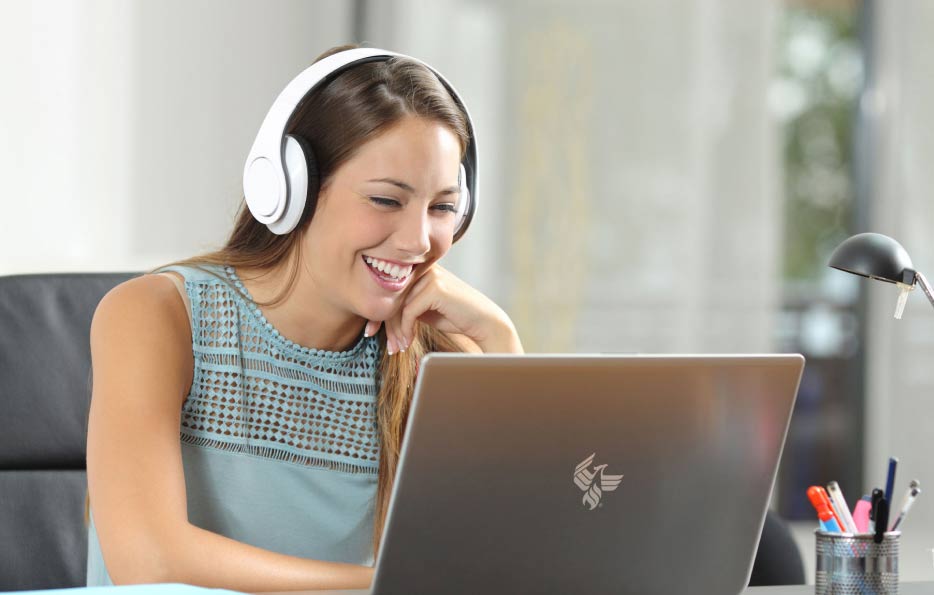 A smiling woman wearing headphones while using a laptop