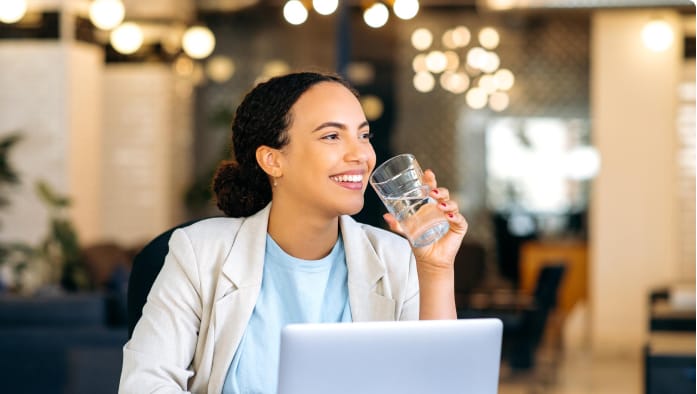 A person takes a break from working at their laptop to drink water.