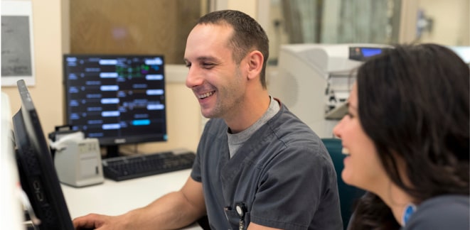 Healthcare worker smiling and working on a computer alongside a coworker