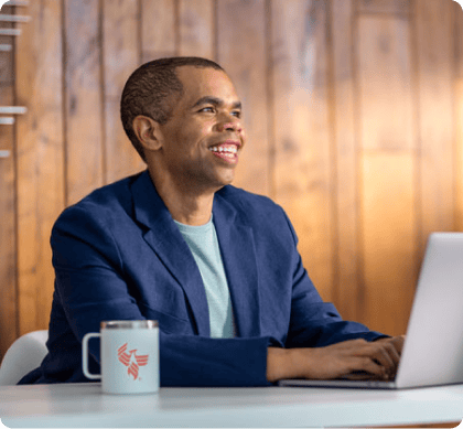 A student smiles while typing on a laptop, preparing a dissertation proposal for an online DBA program.