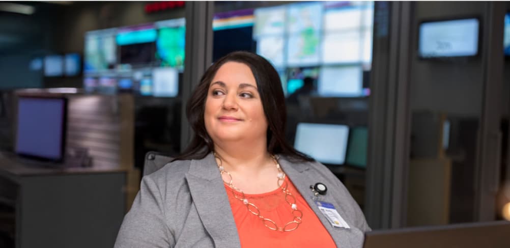 Smiling professional woman in a gray blazer sitting in a command center
