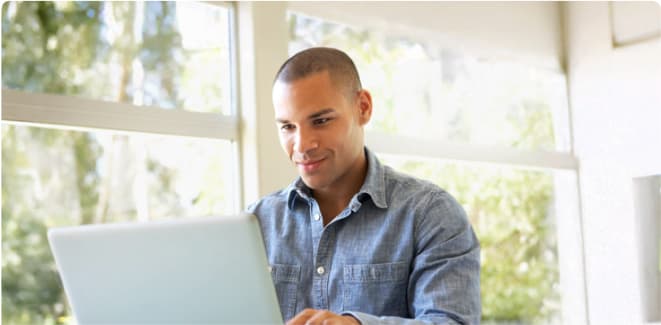 Man working on a laptop at a table by a bright window