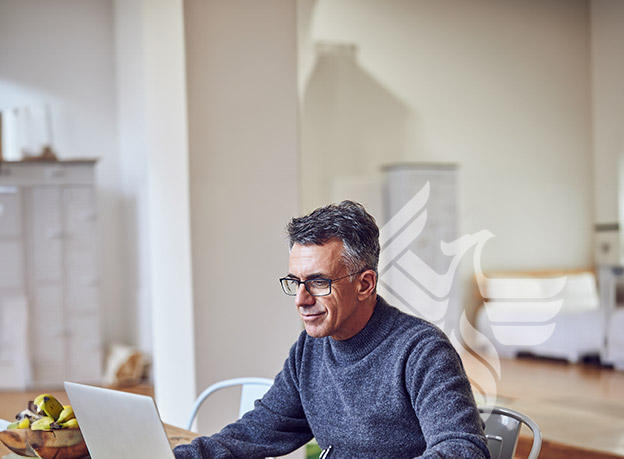 A man in a grey sweater writing on his laptop
