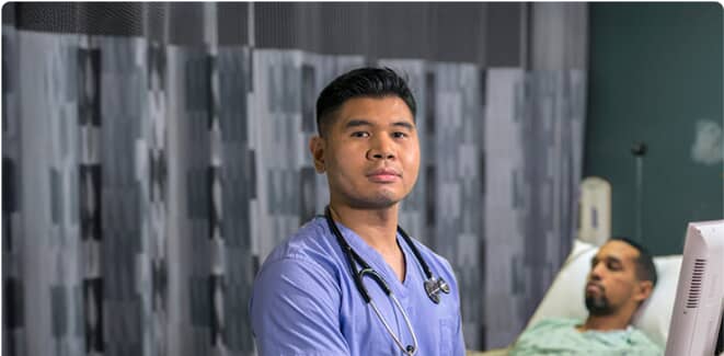 Healthcare worker in blue scrubs smiling while tending to a patient on a bed