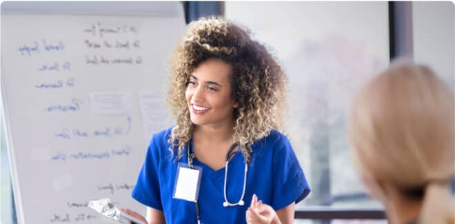 A healthcare worker in blue scrubs smiling while presenting to colleagues