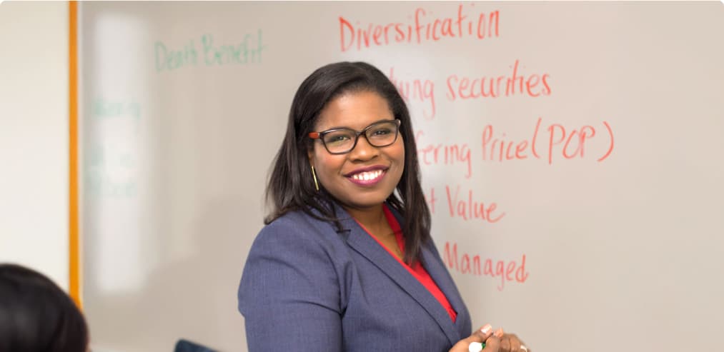 A confident woman in a gray blazer stands by a whiteboard, symbolizing skill development and career growth in a professional setting.