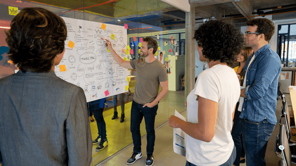 Group of people standing around a whiteboard covered in notes