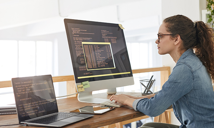 A researcher types at a workstation with monitor and laptop