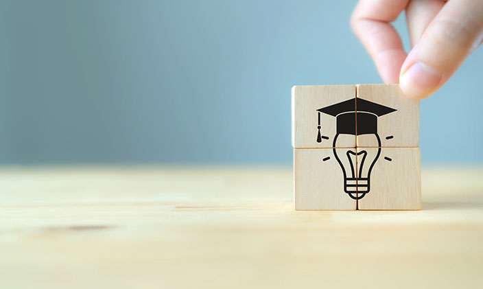 Four wooden tiles are stacked to form a drawing of a lightbulb wearing a mortar board