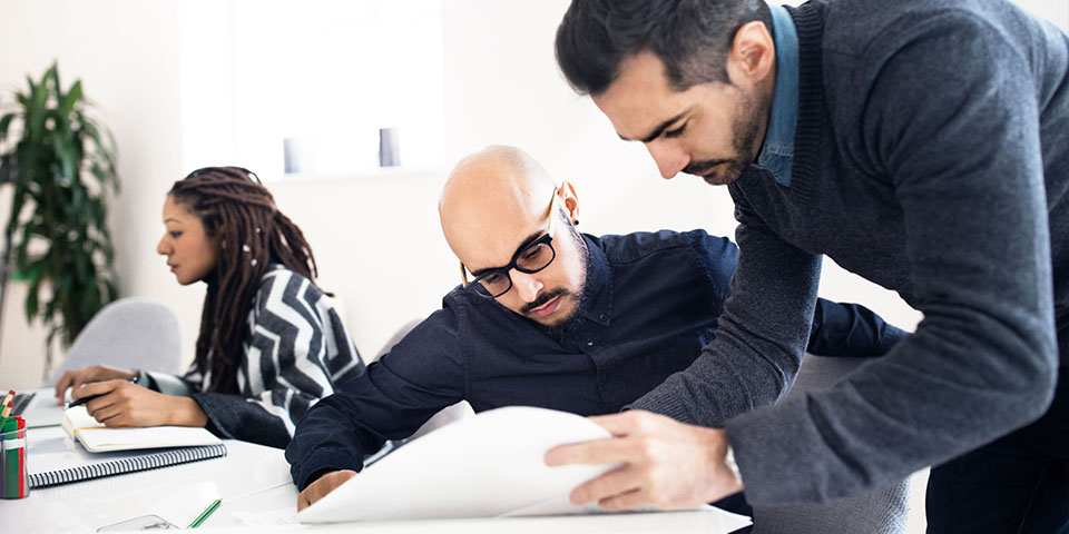 A professor leans over a student as they examine a research paper together