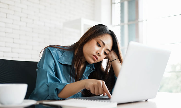 Student slumps over her laptop suffering from self-doubt