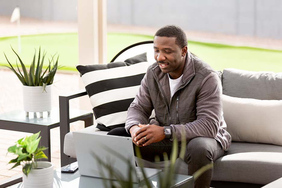 A man talks with colleagues via an online meeting, while sitting on a screened porch
