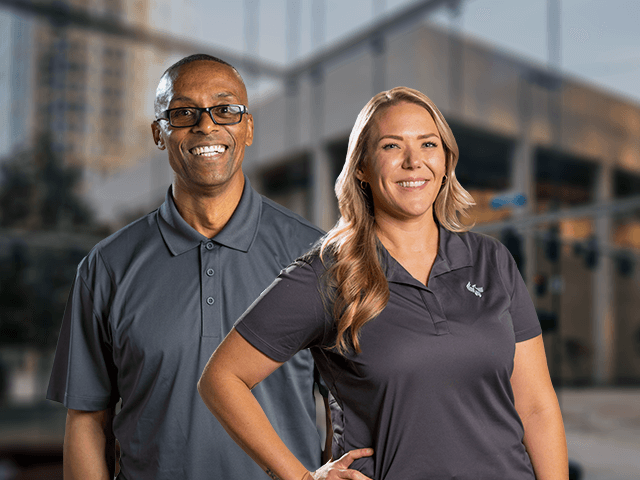 A woman and a man standing next to each other outside, in front of a glass building and smiling.