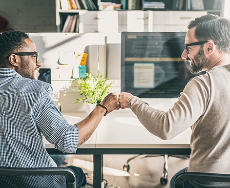 Coworkers fist bumping, sitting at computer