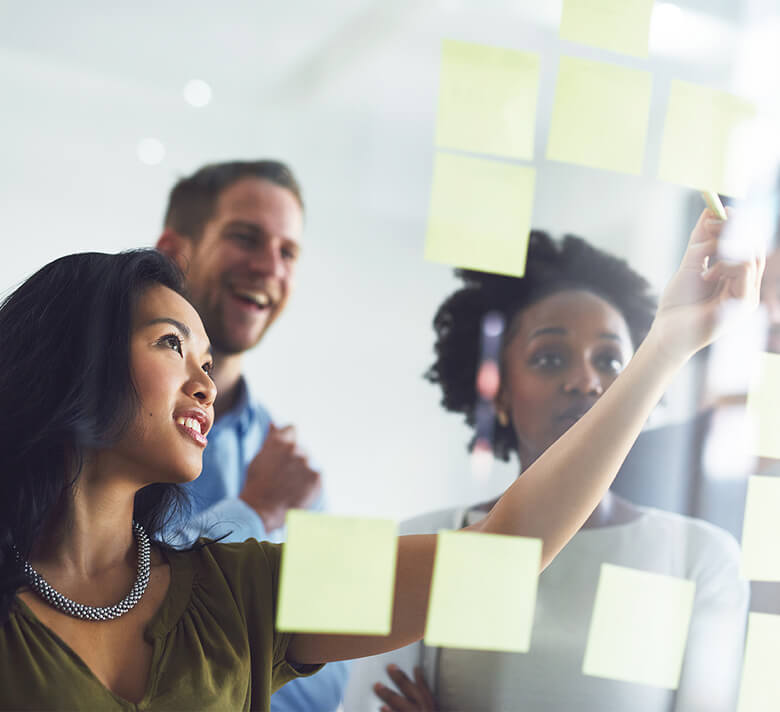 A group of professionals brainstorm on a project using yellow stickies on a glass panel.