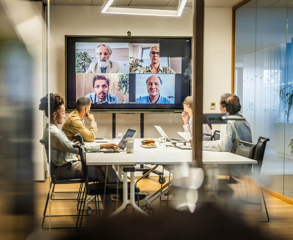 a group of professionals engage in a video confrerence in a glass conference room.