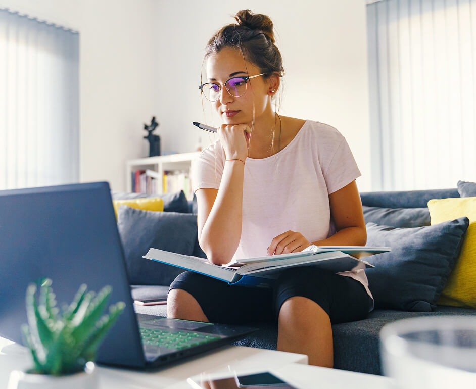 A woman reviews s learning modules with an open textbook and her computer.