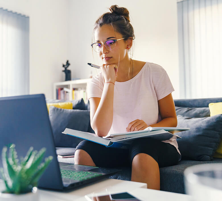 A woman reviews s learning modules with an open textbook and her computer.