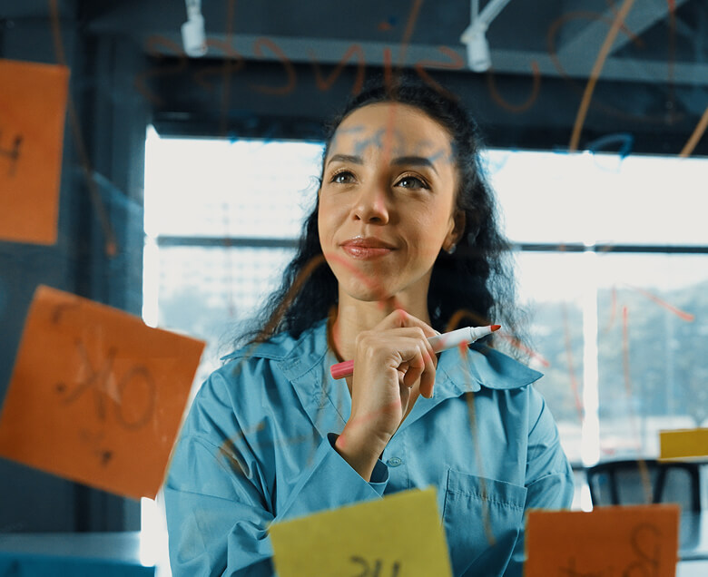 woman reviews ideas posted as orange stickies on a glass panel.