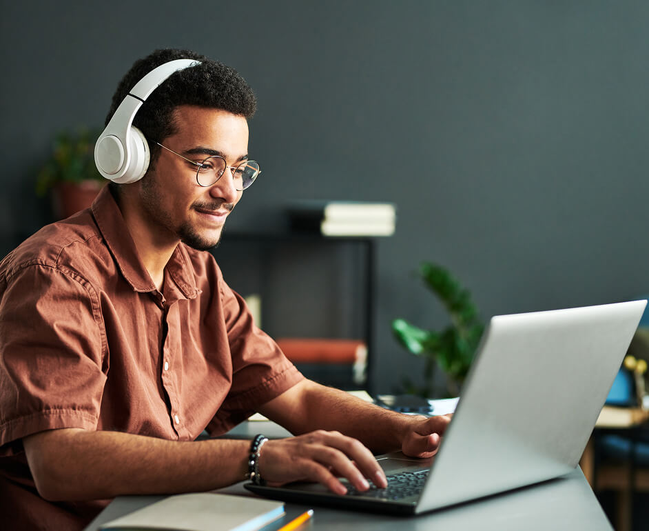 A professional listens to learning modules on headphones while reviewing learnng materials on his laptop.