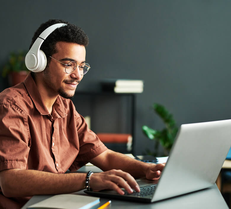 A professional listens to learning modules on headphones while reviewing learnng materials on his laptop.